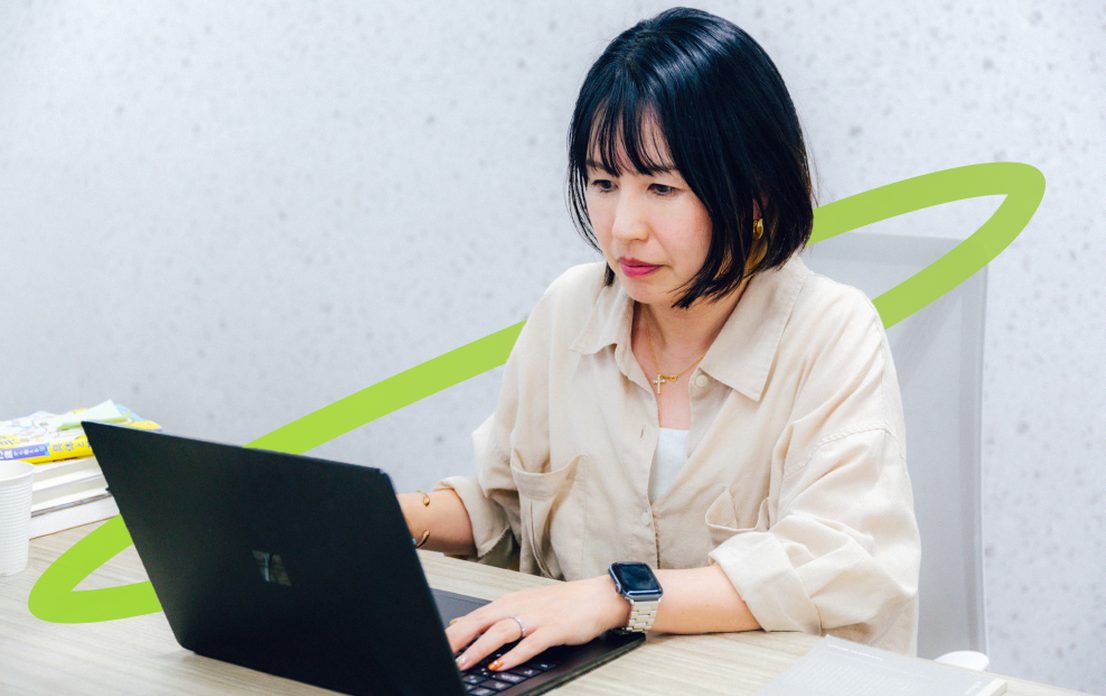 資料を横に置いてノートPCで作業する社員